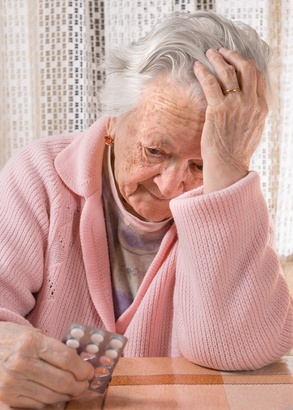 Old sad woman holding pills at home